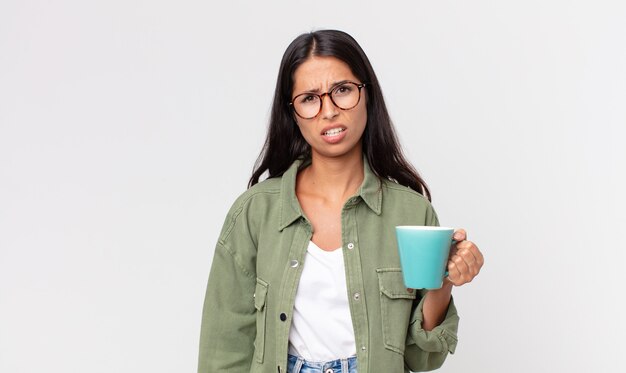 Joven hispana sintiéndose desconcertado y confundido y sosteniendo una taza de café