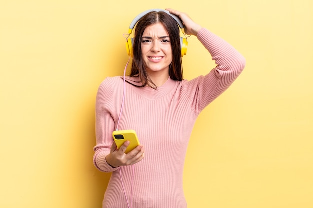 Foto joven hispana sintiéndose estresada, ansiosa o asustada, con las manos en la cabeza. concepto de auriculares y teléfono