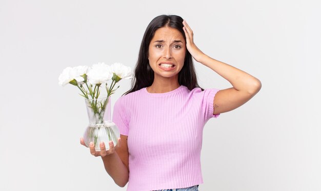 Joven hispana sintiéndose estresada, ansiosa o asustada, con las manos en la cabeza sosteniendo flores decorativas