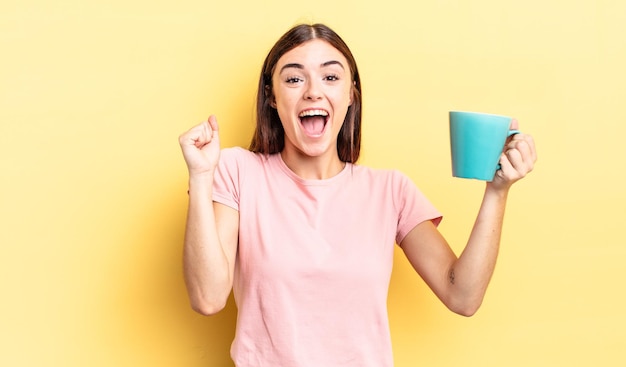 Joven hispana sintiéndose sorprendida riéndose y celebrando el concepto de taza de café de éxito