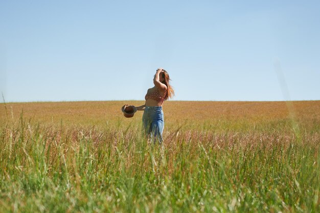 Joven hispana con sombrero posando en un campo de trigo en un día soleado