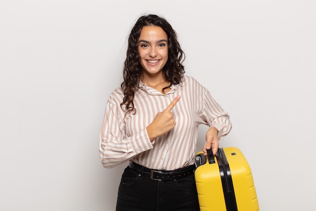 Joven hispana sonriendo alegremente, sintiéndose feliz y apuntando hacia un lado y hacia arriba, mostrando el objeto en el espacio de la copia