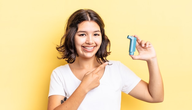 Joven hispana sonriendo alegremente, sintiéndose feliz y apuntando hacia un lado. concepto de asma