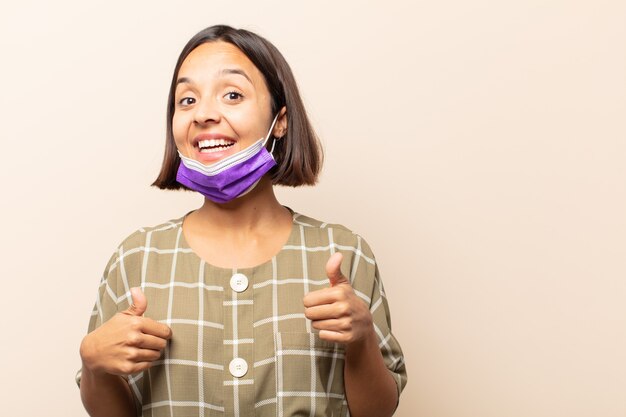 Joven hispana sonriendo ampliamente mirando feliz, positivo, seguro y exitoso, con ambos pulgares hacia arriba