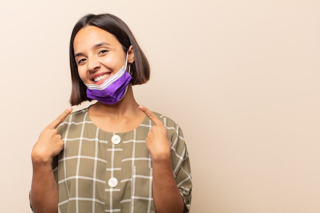 Joven hispana sonriendo con confianza apuntando a su propia sonrisa amplia, actitud positiva, relajada y satisfecha