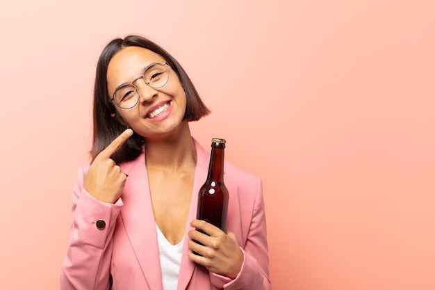 Joven hispana sonriendo con confianza apuntando a su propia sonrisa amplia, actitud positiva, relajada y satisfecha