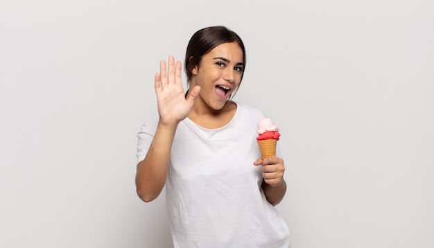 Joven hispana sonriendo feliz y alegremente, saludando con la mano, dándote la bienvenida y saludándote, o diciéndote adiós