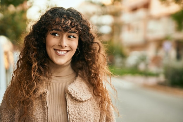 Joven hispana sonriendo feliz de pie en la ciudad