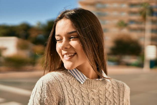 Joven hispana sonriendo feliz de pie en la ciudad