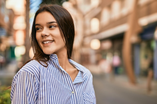 Joven hispana sonriendo feliz de pie en la ciudad