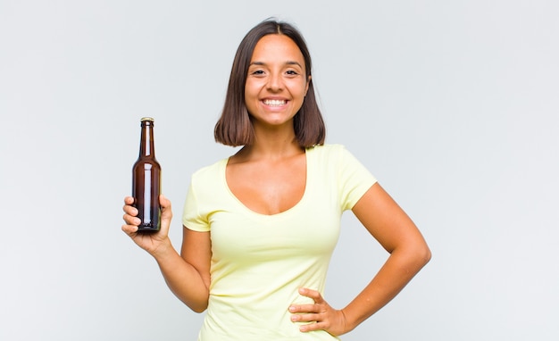 Foto joven hispana sonriendo felizmente con una mano en la cadera y actitud confiada, positiva, orgullosa y amistosa