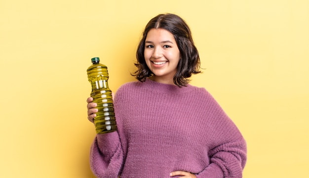 Joven hispana sonriendo felizmente con una mano en la cadera y confiada. concepto de aceite de oliva