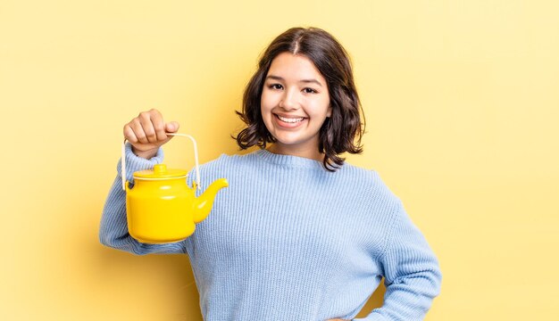 Joven hispana sonriendo felizmente con una mano en la cadera y confiada. concepto de tetera