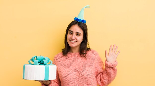 Joven hispana sonriendo felizmente saludando con la mano dándole la bienvenida y saludando su concepto de cumpleaños