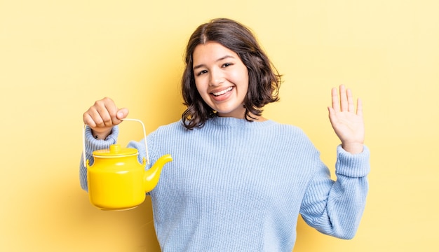 Joven hispana sonriendo felizmente, saludando con la mano, dándote la bienvenida y saludándote. concepto de tetera