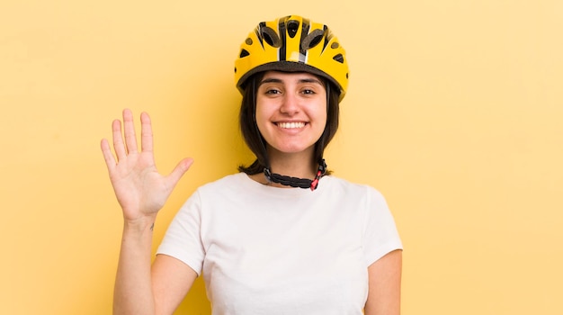 Joven hispana sonriendo y luciendo amigable mostrando el concepto de casco de bicicleta número cinco