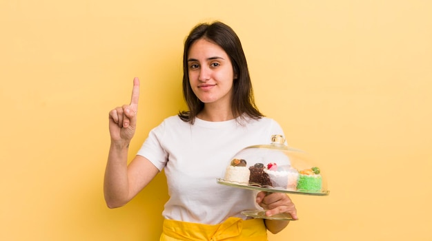 Joven hispana sonriendo y luciendo amigable mostrando el concepto de pasteles caseros número uno