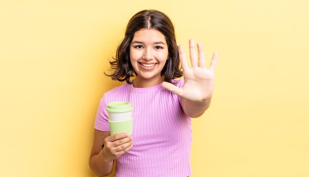 Joven hispana sonriendo y luciendo amigable, mostrando el número cinco. concepto de café para llevar