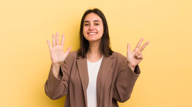 Joven hispana sonriendo y luciendo amigable mostrando el número ocho u octavo con la mano hacia adelante contando hacia atrás