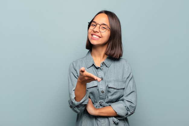 Joven hispana sonriendo, luciendo feliz, confiada y amigable, ofreciendo un apretón de manos para cerrar un trato, cooperando