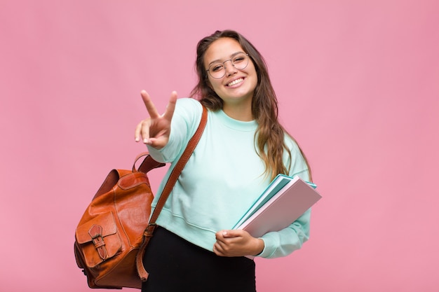 Joven hispana sonriendo y luciendo feliz, despreocupada y positiva, gesticulando victoria o paz con una mano