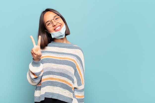 Joven hispana sonriendo y luciendo feliz, despreocupada y positiva, gesticulando victoria o paz con una mano