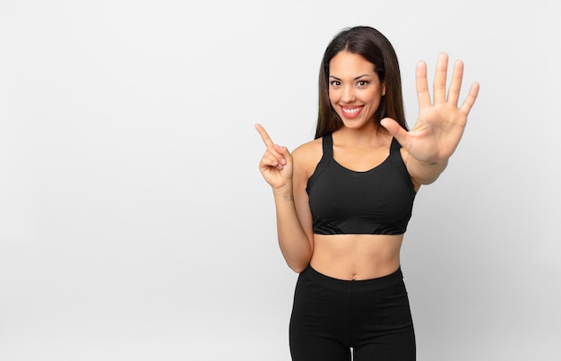 joven hispana sonriendo y mirando amigable, mostrando el número cinco. concepto de fitness