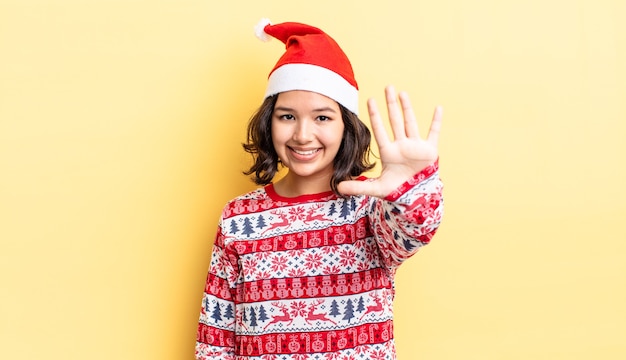 Joven hispana sonriendo y mirando amigable, mostrando el número cinco. concepto de navidad