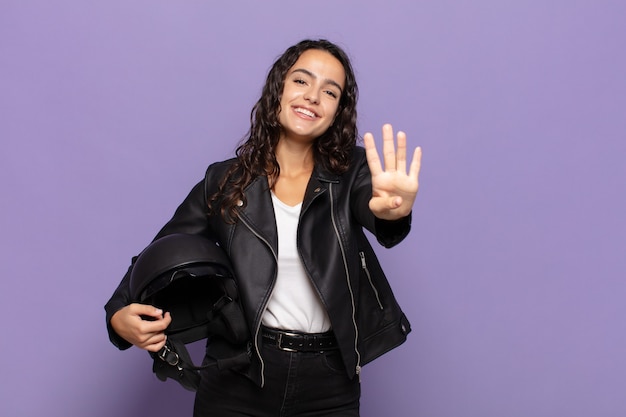 Joven hispana sonriendo y mirando amistosamente, mostrando el número cuatro o cuarto con la mano hacia adelante, contando hacia atrás