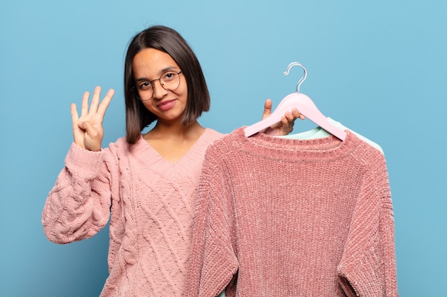 Foto joven hispana sonriendo y mirando amistosamente, mostrando el número cuatro o cuarto con la mano hacia adelante, contando hacia atrás