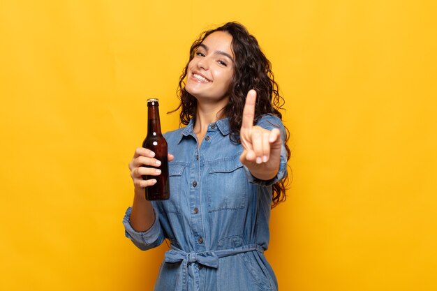 Foto joven hispana sonriendo con orgullo y confianza haciendo la pose número uno triunfalmente, sintiéndose como una líder