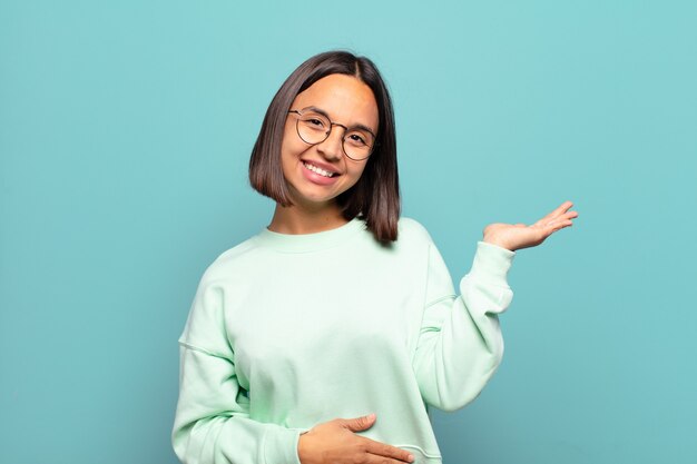 Joven hispana sonriendo, sintiéndose confiada, exitosa y feliz, mostrando concepto o idea en el espacio de la copia en el lateral