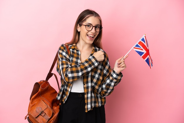 Joven hispana sosteniendo una bandera del Reino Unido aislada en la pared rosa celebrando una victoria