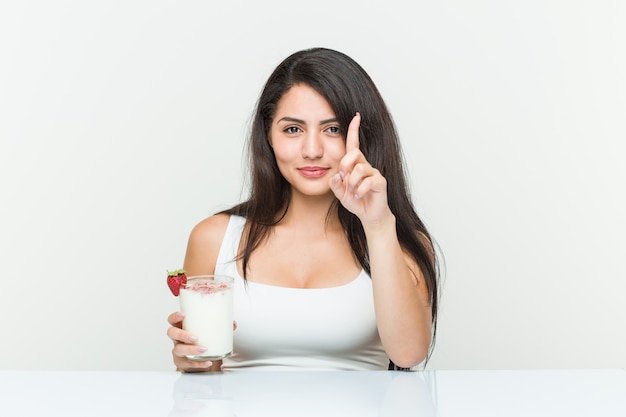 Joven hispana sosteniendo un batido Joven hispana sosteniendo una tostada de aguacate mostrando el número uno con el dedo. <Mixto>