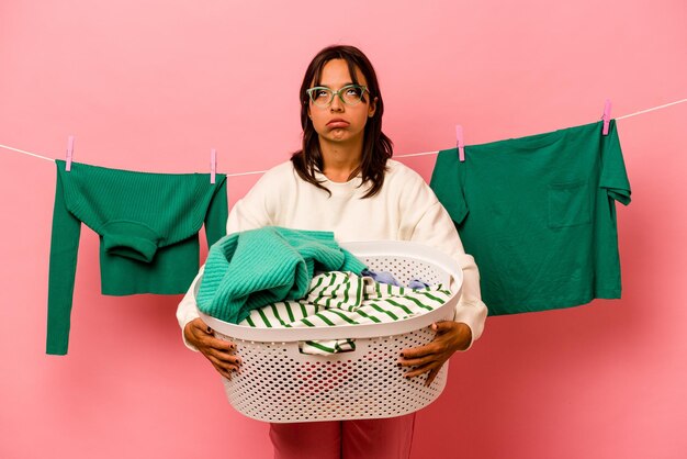 Joven hispana sosteniendo una cesta de ropa aislada de fondo rosa