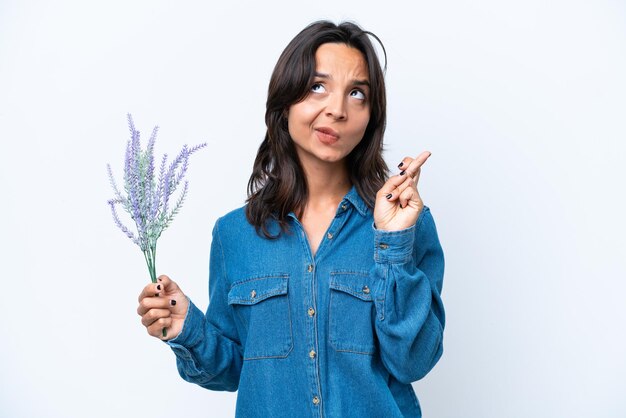 Joven hispana sosteniendo lavanda aislada de fondo blanco con los dedos cruzados y deseando lo mejor