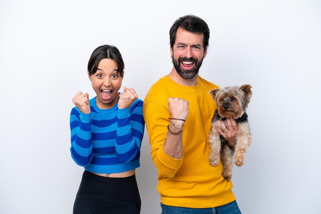 Joven hispana sosteniendo un perro aislado de fondo blanco celebrando una victoria