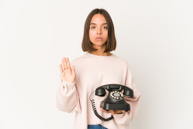 Foto joven hispana sosteniendo un teléfono vintage aislado de pie con la mano extendida mostrando la señal de stop, impidiéndote.