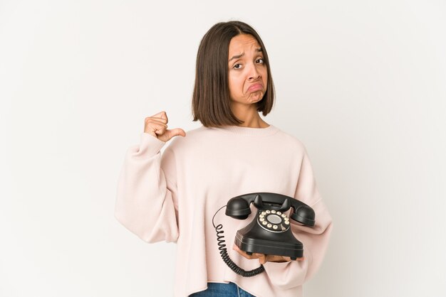 Joven hispana sosteniendo un teléfono vintage aislado se siente orgullosa y segura de sí misma, ejemplo a seguir.