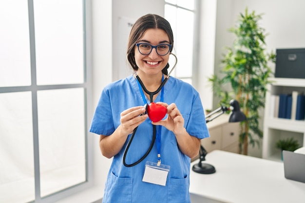 Joven hispana con uniforme médico auscultando el corazón en la clínica