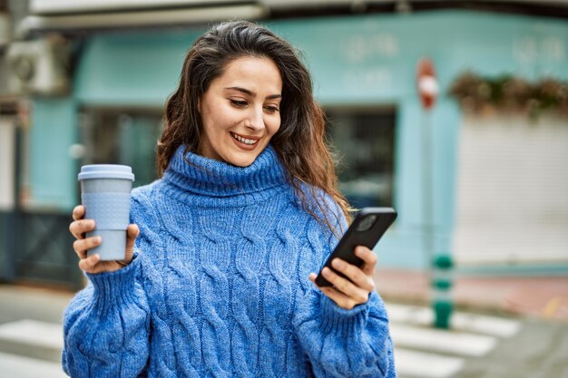 Joven hispana usando un teléfono inteligente tomando café en la ciudad.