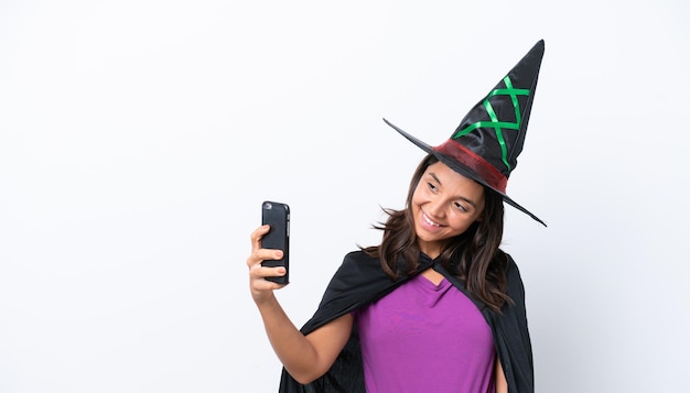 Joven hispana vestida de bruja sobre un fondo aislado haciendo un selfie