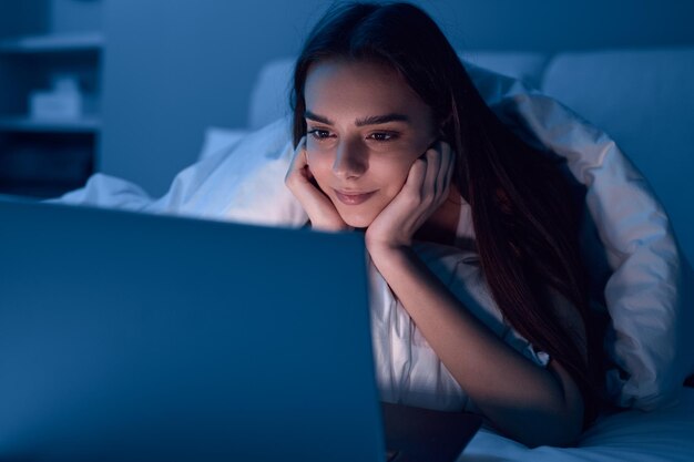 Joven hispana viendo videos en una laptop mientras descansa en la cama