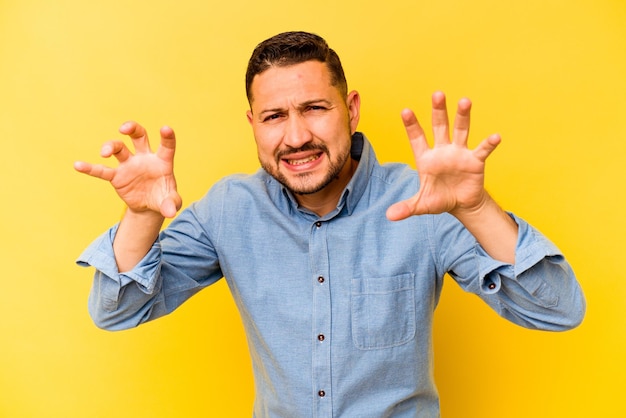 Joven hispano aislado de fondo amarillo molesto gritando con las manos tensas