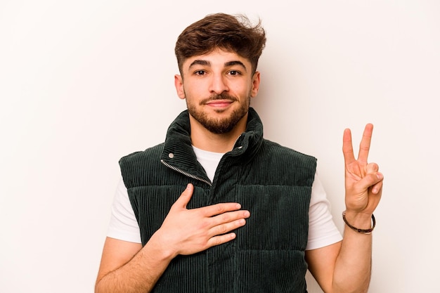 Joven hispano aislado de fondo blanco haciendo un juramento poniendo la mano en el pecho