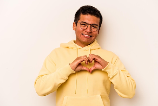 Joven hispano aislado de fondo blanco sonriendo y mostrando una forma de corazón con las manos