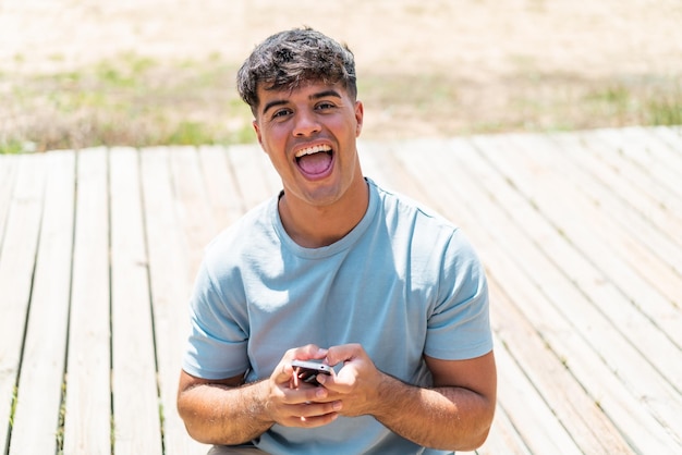 Joven hispano al aire libre sorprendido y enviando un mensaje