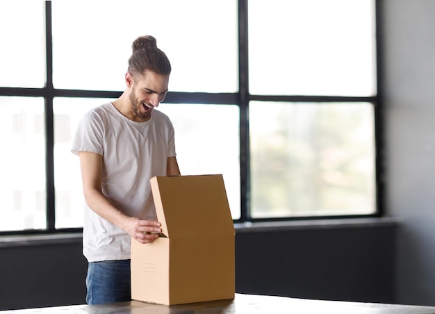 Foto joven hispano alegre abriendo una caja desempaquetando un paquete en el lugar de trabajo