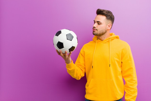 Joven hispano con un balón de fútbol contra la pared púrpura