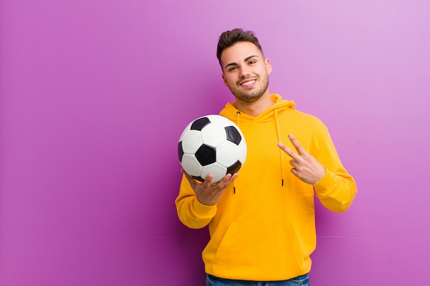 Joven hispano con un balón de fútbol contra púrpura